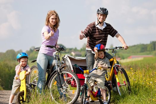 Family with two children having a weekend excursion on their bikes on a summer day in beautiful landscape, for safety and protection they are wearing helmets