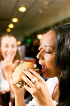 Friends - one couple is African American - eating hamburger and drinking soda in a fast food diner; focus on the woman in front