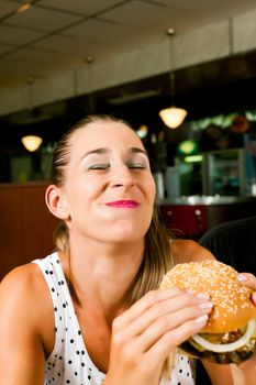 Happy woman in a fast food restaurant eating a hamburger and seems to enjoy it