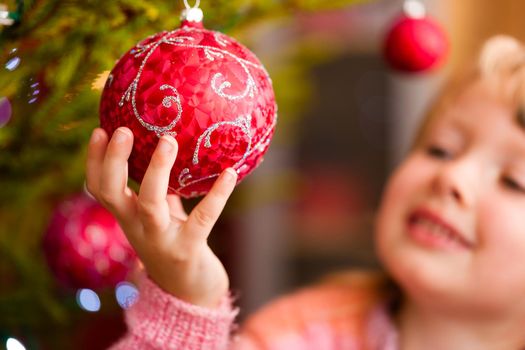 Young girl helping decorating the Christmas tree, holding some Christmas baubles in her hand