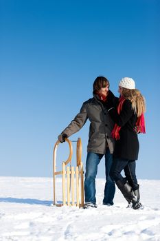 Happy couple in winter with sled in the snow