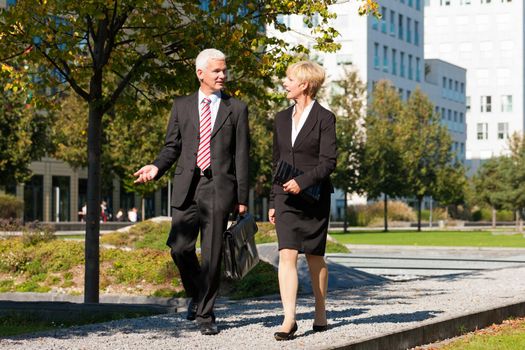 Business people - mature or senior - talking outdoors and walking in a park