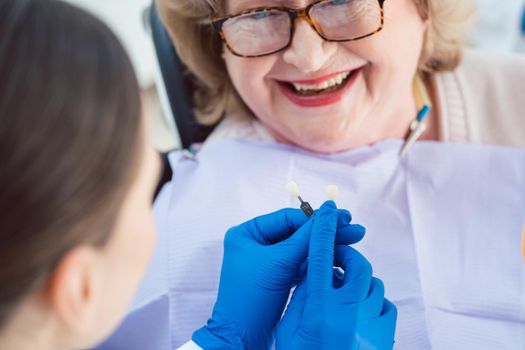 Dentist woman performing dental bleaching at senior patient showing possible outcomes