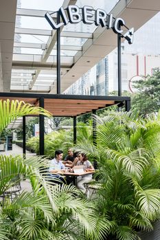 People sitting down at tables outdoors at a modern cafeteria surrounded by green vegetation in Asia