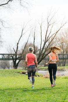 Senior woman with daughter running along the river away from the viewer