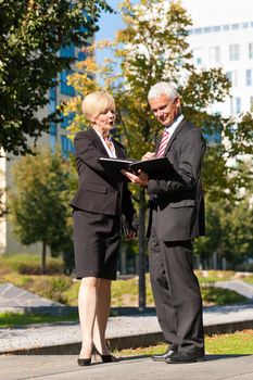 Business people - mature or senior - talking outdoors and discussing a document