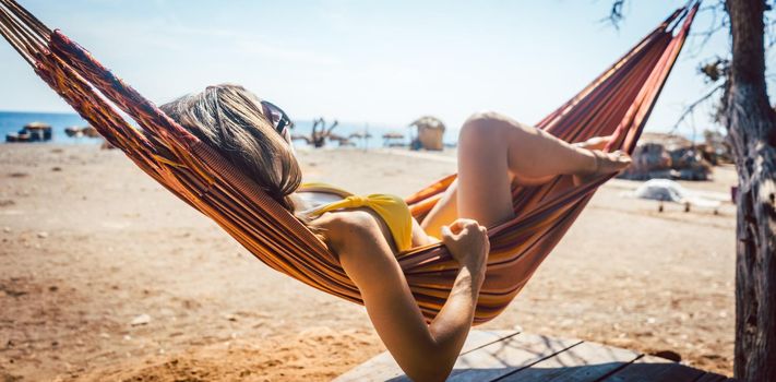 Woman lying in hammock close to the beach enjoying the sun