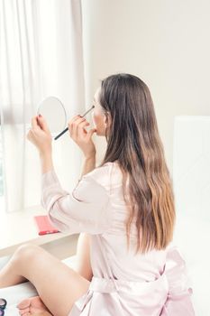Woman applying makeup in her bedroom in the morning looing in the mirror