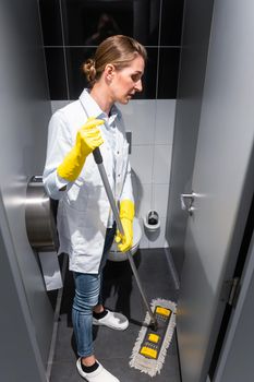 Cleaning lady or janitor mopping the floor in restroom cleaning the stall