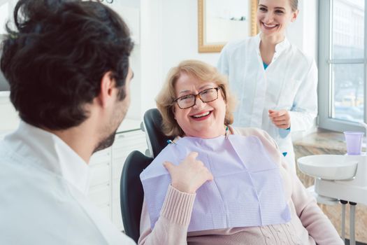 Dentist and assistant greeting senior patient in their surgery