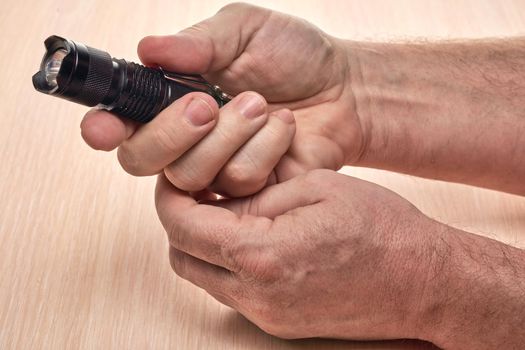 Hands hold a small black flashlight to replace the used battery. Close up