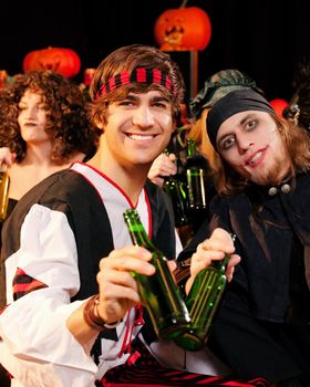 Group of young people celebrating a carnival or Halloween party in costumes drinking beer