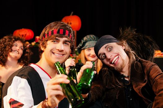 Group of young people celebrating a carnival or Halloween party in costumes drinking beer