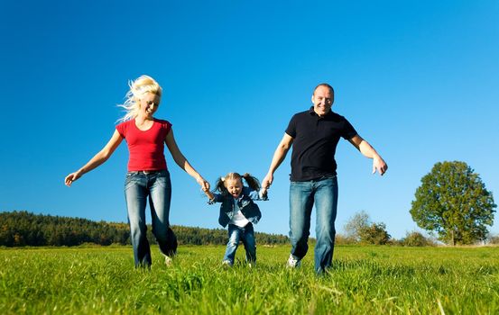 Young family having fun in the sun running over the meadow an a bright summer day