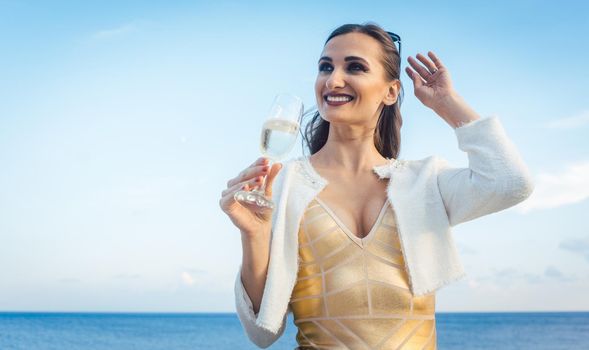 Woman sitting by the sea at a party on beach with glass of Champagne