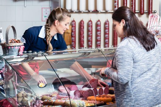 Sales lady in butchery shop serving customer selling meat