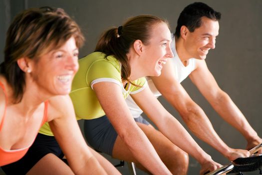 Three people spinning on stationary bicycles in a gym or fitness club; focus on girl in the middle