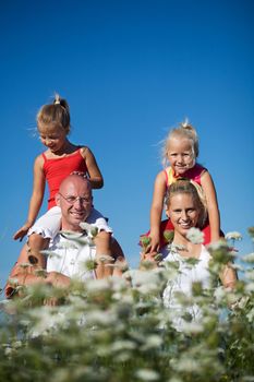 A young family with two cute daughters sitting on the shoulders of the parents, this in a field of yarrow