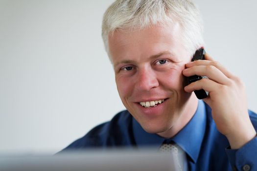 Portrait of a businessman on the phone, looking at the viewer over his laptop computer