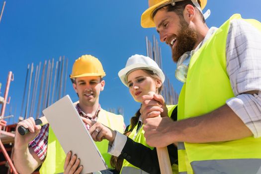 Low-angle view of a female architect or manager showing to her colleagues the electronic plan of the building on a tablet, during work on the construction site