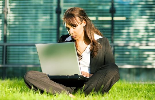 Female professional with a laptop on the lawn in front of a glass and steel facade