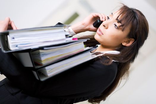 An unhappy female office employee carrying files and using cell phone simultaneously