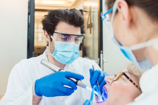 Dentists hardening toot crown with UV light treating senior patient