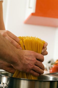 Man - only hands to be seen - is stirring pasta cooking in hot water in a pot