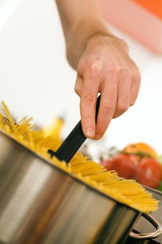 Woman - only hands to be seen - is stirring pasta cooking in hot water in a pot