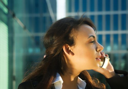 Attractive young female professional catching the last rays of the evening sun using her mobile in front of an office building