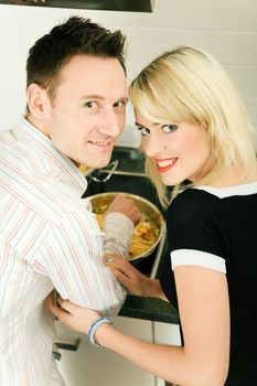 Young couple cooking in their kitchen at home, both looking into the camera