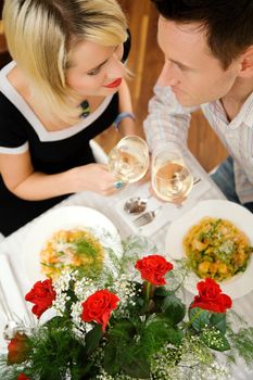 Young couple romantic dinner: letting the white wine glasses clink; focus on the eyes of the people