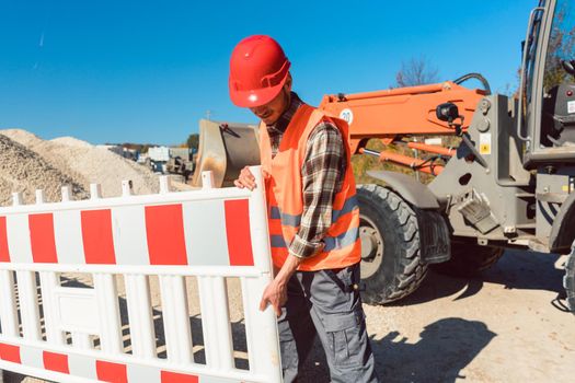 Worker setting up earthworks construction site erecting fence