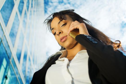 A brunette woman in business clothes using her mobile in front of a modern business building