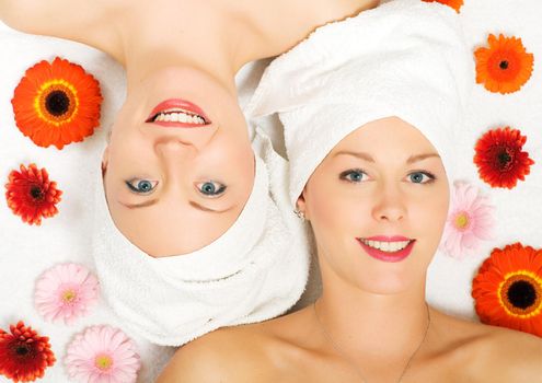 Two girls relaxing in a wellness set-up seen from above, vertically aligned, with some flowers, open eyes, smiling