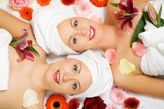 Two girls relaxing in a wellness set-up seen from above, horizontally aligned, with lots of flowers, open eyes, smiling