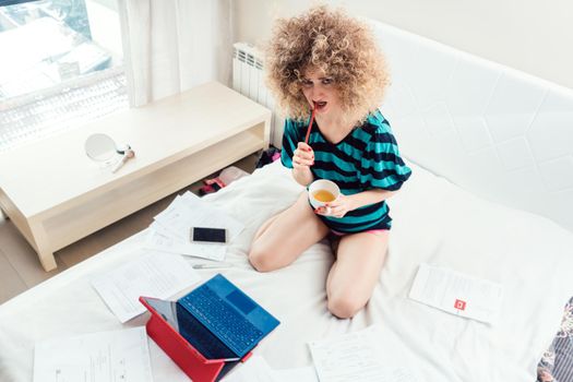 Woman working on her bed with laptop looking puzzled