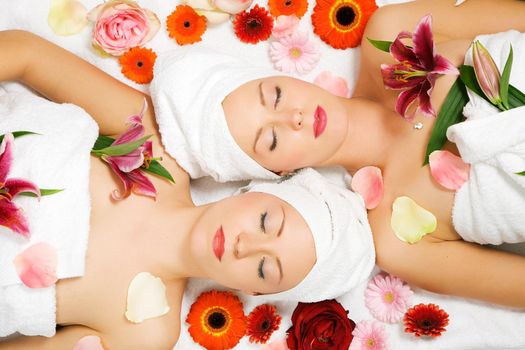 Two girls relaxing in a wellness set-up seen from above, horizontally aligned, with lots of flowers, closed eyes