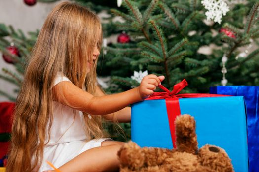 Cute Child with teddy bear toy finding her Christmas present in the morning still in her sleepwear and unwrapping it