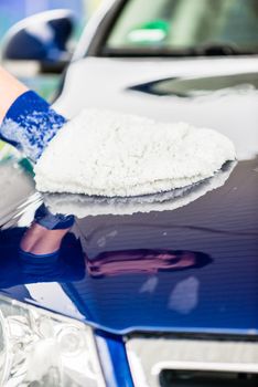 Man polishing the bonnet of his luxury blue car, using a soft glove or mitt in a close up view of his hand with copy space