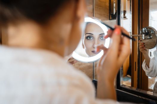 Young woman in hotel bathroom doing her makeup looking at the mirror