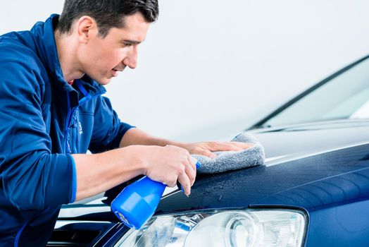 Proud car owner cleaning his vehicle with a sponge and detergent in a spray bottle , close up cropped profile view