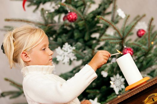 Child lighting Christmas candles in front of a Christmas tree