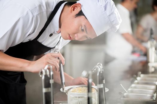 Young Asian chef plating food in a restaurant carefully pipetting garnish onto the side of a plate