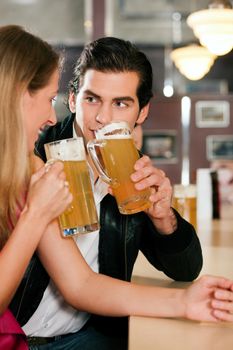 Group of people in a bar or restaurant drinking beer, one couple flirting very obviously having a lot of fun