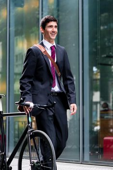 Businessman walking through town wheeling his bicycle along a pedestrian walkway past a commercial building with a smile on his face