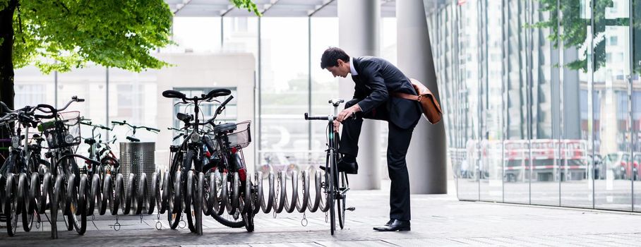 Businessman parking his bicycle in town at a bicycle rack after commuting to work in a concept of eco-friendly transport and healthy active lifestyle, panoramic banner view