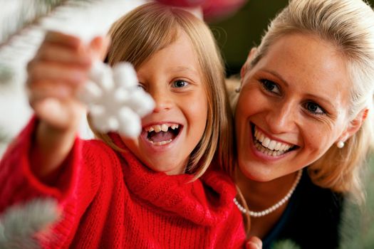 Young girl helping her father decorating the Christmas tree, holding some Christmas baubles in her hand (Focus on child)