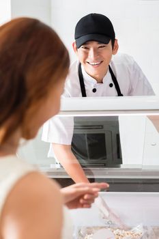 Smiling helpful assistant serving a female customer to food in a delicatessen as she points to her choice in a glass counter