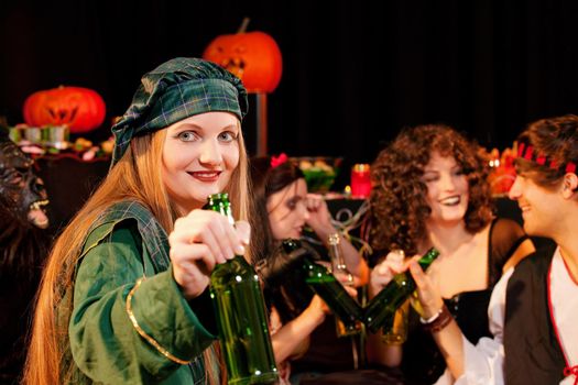 Group of young people celebrating a carnival or Halloween party in costumes drinking beer